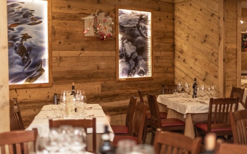 Elegant dining room with two tables set for dinner, featuring artwork and a warm wood-paneled atmosphere.