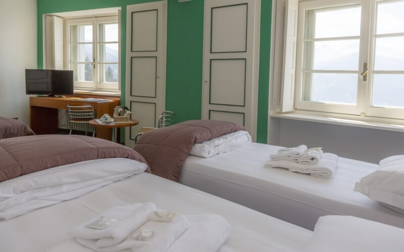 Hotel room with two twin beds, a desk with a kettle and teacups, and windows, featuring green walls and white doors.