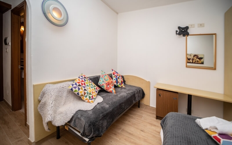 Camera degli ospiti accogliente con letto, cuscini colorati, pavimento in legno e specchio, ideale per la serenità.