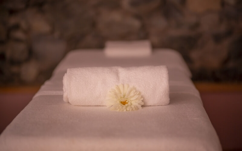 Serene spa bed with white towels and an artificial flower, exuding relaxation in a softly lit environment.