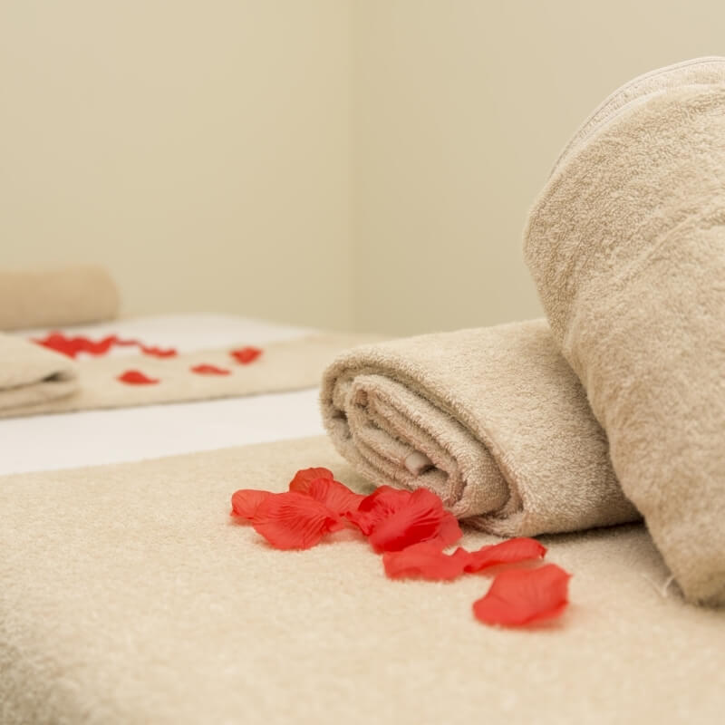 Neatly arranged rolled towels with red flower petals on a white surface, creating a serene spa atmosphere.