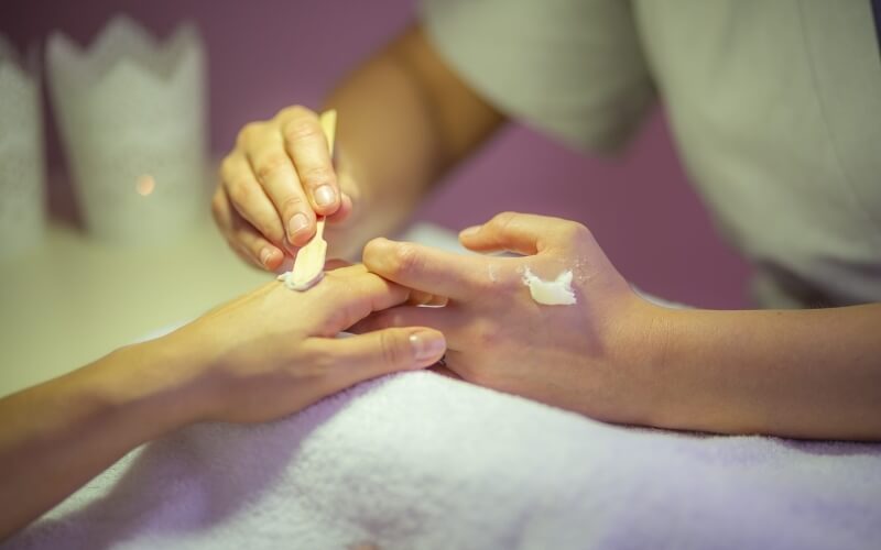 Close-up of a manicure treatment with a technician applying cuticle oil to a client's hands on a white towel.