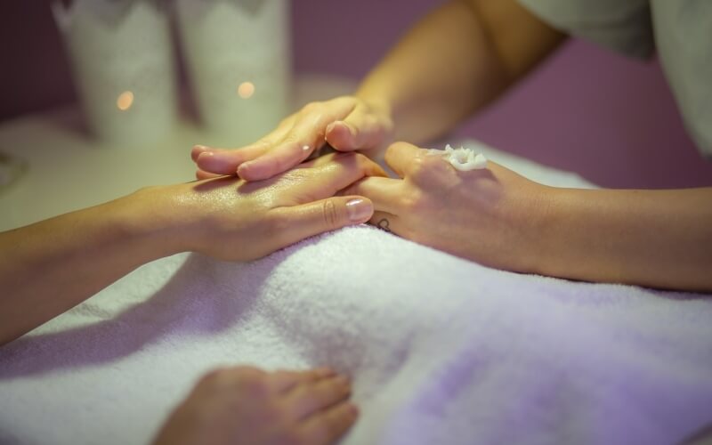 A person receives a hand massage, with a tattoo visible on their left ring finger, in a spa-like setting with candles.