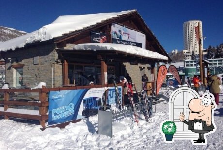 Building with snow-covered roof, sign "For Super-Igloo," people outside, skis by a wooden fence, and a cartoon character with a plant.