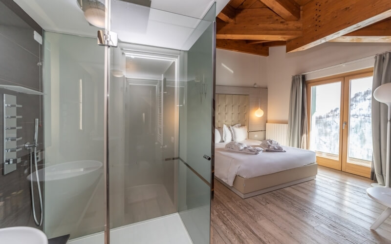 Image of a modern bathroom with a glass shower and a cozy bedroom featuring a plush bed and mountain views.