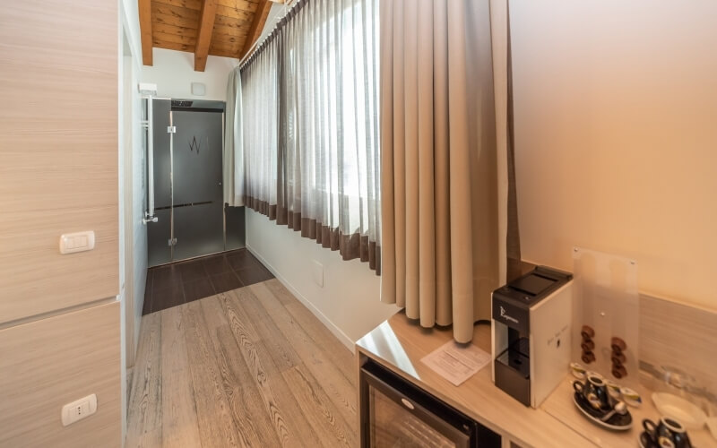 Wooden-floored hallway with a glass door, white walls, beige curtains, and a counter with a coffee maker and cups.