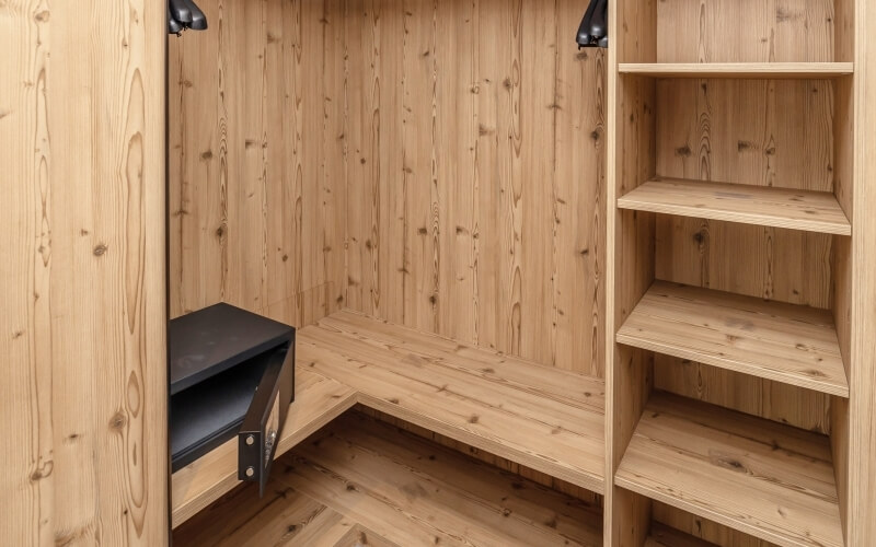 A minimalist room with light wood paneling, featuring a black shelf on the left and four empty wooden shelves on the right.