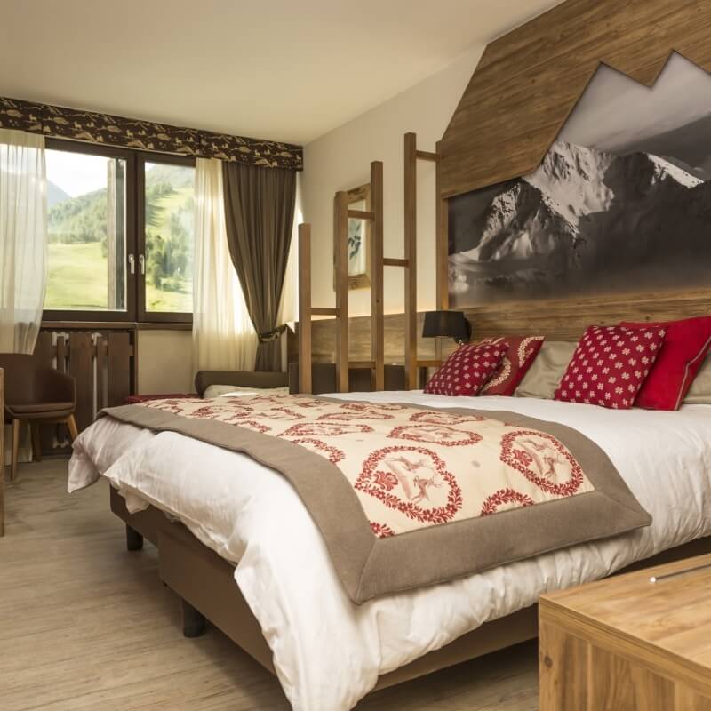 Cozy bedroom with mountain-themed decor, featuring a bed, nightstand, chair, and a window with a serene outdoor view.