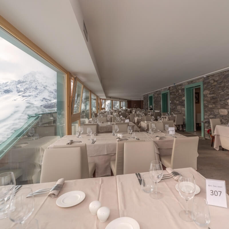 Spacious dining room with mountain views, elegantly set tables, and a rustic stone accent wall, creating a warm atmosphere.