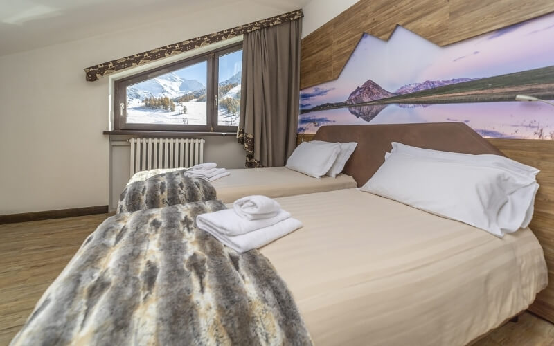 Cozy hotel room with two double beds, mountain view, beige decor, and warm tones, creating a serene ambiance.