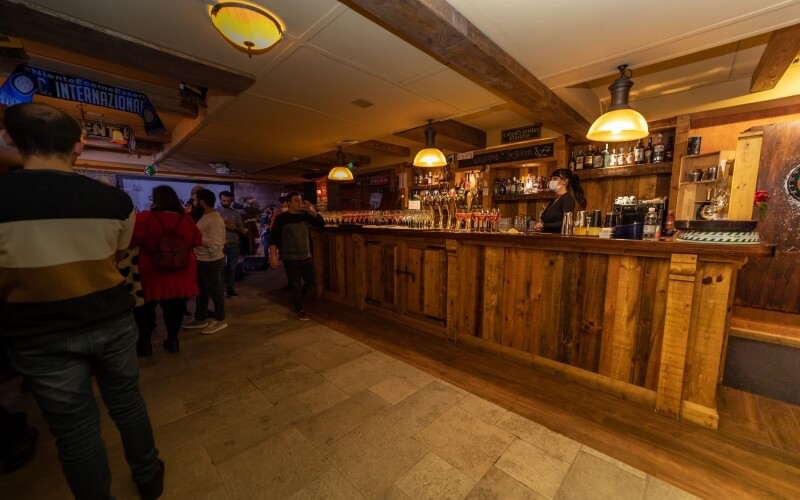 A lively bar scene with patrons at the counter, a bartender serving drinks, and a sign reading "International" above.