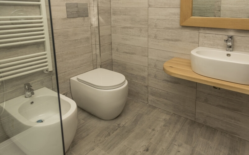 Modern minimalist bathroom with light wood paneling, white bidet and toilet, wooden countertop sink, and mirror.