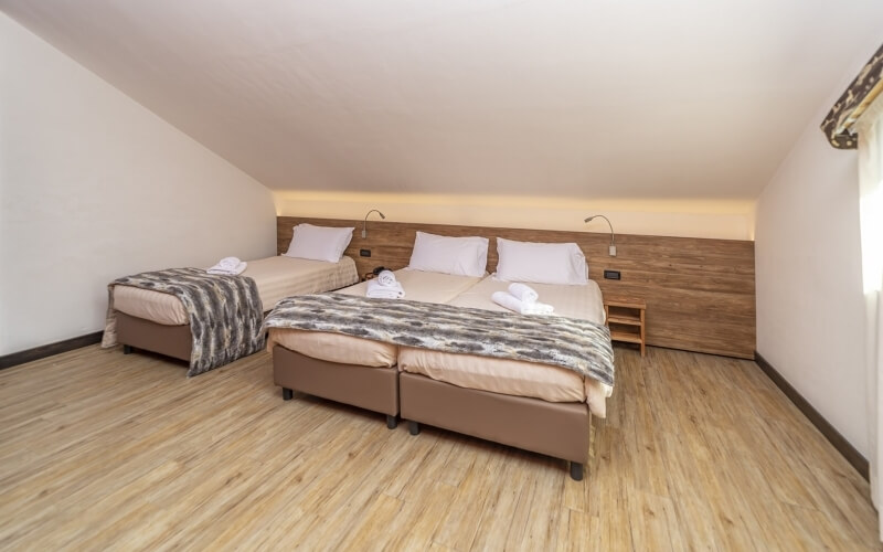 Spacious room with two beds, wooden floor, warm lighting, and rustic wall, creating a calm and inviting atmosphere.