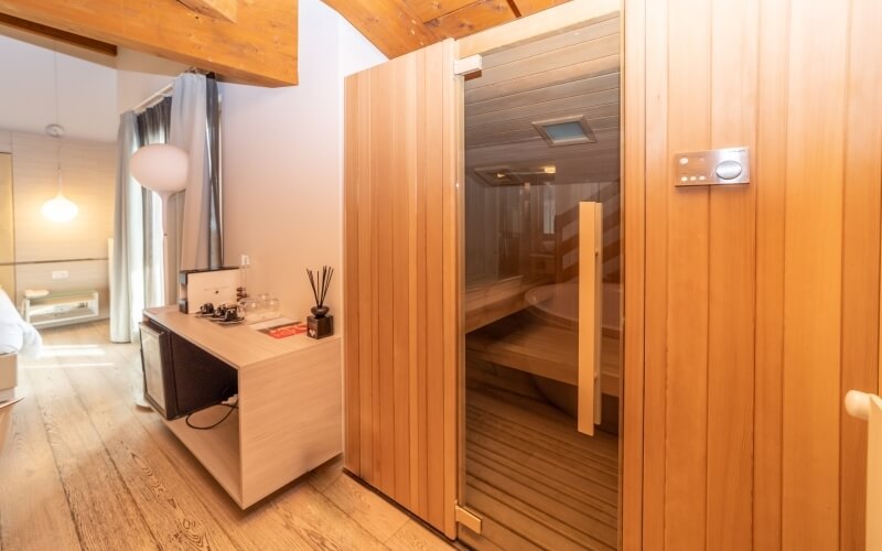 A serene spa room featuring a wooden desk, sauna with glass door, and calming white walls and hardwood floor.