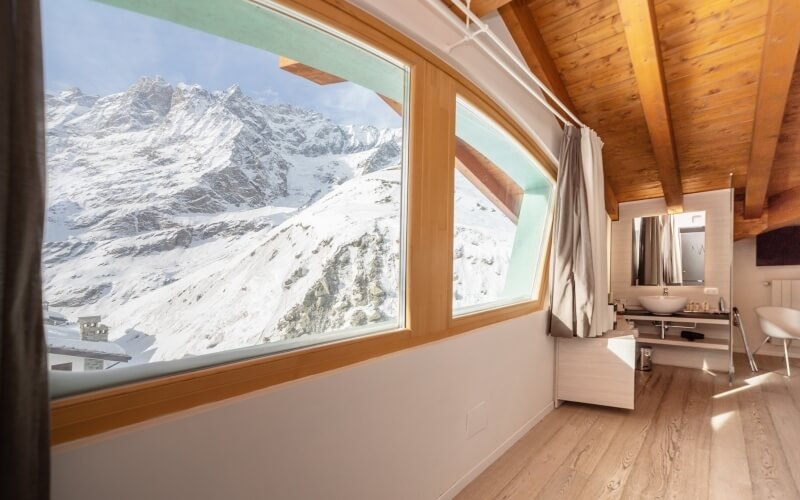 Bathroom with a large window revealing snow-capped mountains, light wood decor, and a serene atmosphere.