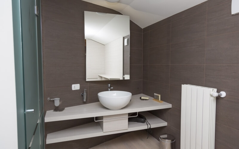 Modern bathroom with a white sink, mirror, towel rack, and dark brown tiled walls, featuring a minimalist design.