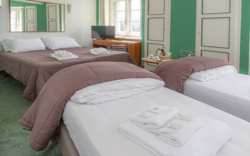 Hotel room with three neatly made beds, brown and white bedding, a television, and green and white walls.