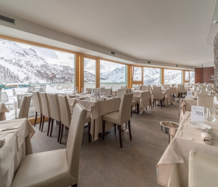 Elegant dining room with white decor, large windows showcasing snow-covered mountains, and tables set for fine dining.