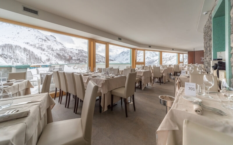 Elegant restaurant with white tablecloths, mountain views through large windows, and natural lighting.