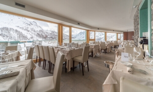 Spacious dining area with long tables, mountain views through large windows, and elegant table settings in a cozy atmosphere.