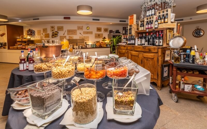 Breakfast buffet featuring granola, pastries, fruits, and condiments on blue tablecloths in a warm restaurant setting.