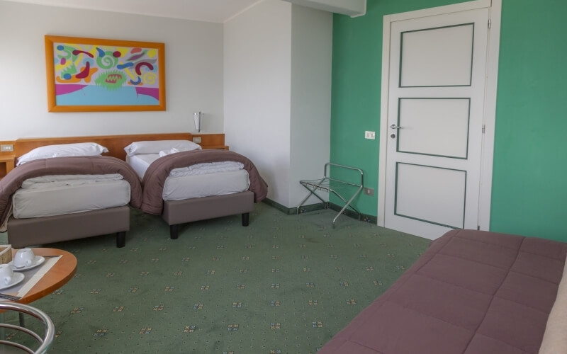 Modern hotel room with two beds, a round table, colorful wall art, and green carpet.