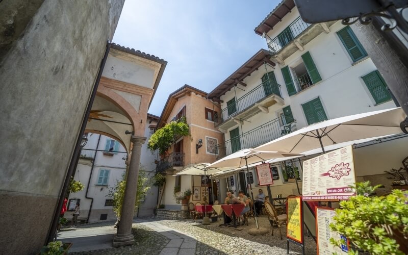 Charming Italian courtyard with pastel buildings, outdoor seating, stone archway, and bright blue sky, evoking warmth and hospitality.