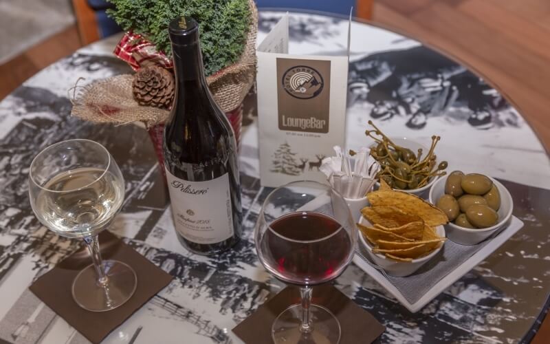 A table with wine glasses, a bottle of red wine, snacks, and a plant, set for a casual gathering.