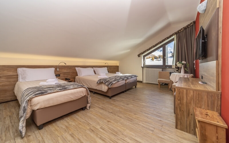 Hotel room with two beige beds, a window, wooden floor, desk, chair, and TV, exuding comfort and tranquility.