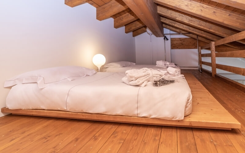 Dimly lit attic bedroom with a wooden bed, soft lighting, and a shelf displaying freshly folded clothes.