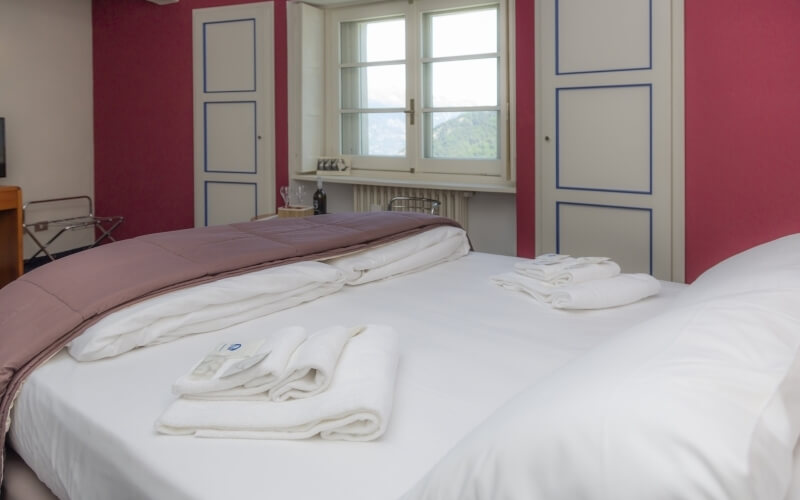 Hotel bedroom with two single beds, red walls, blue-trimmed cupboards, luggage rack, and a TV on a wooden table.