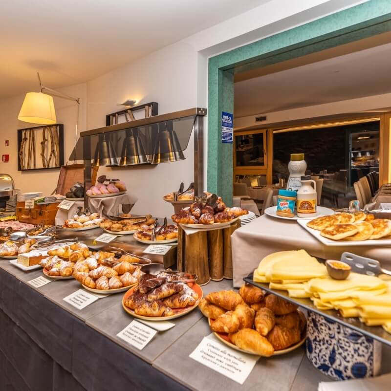 Breakfast buffet featuring pastries, cheeses, pancakes, and fruit in a room with white walls and a hanging lamp.