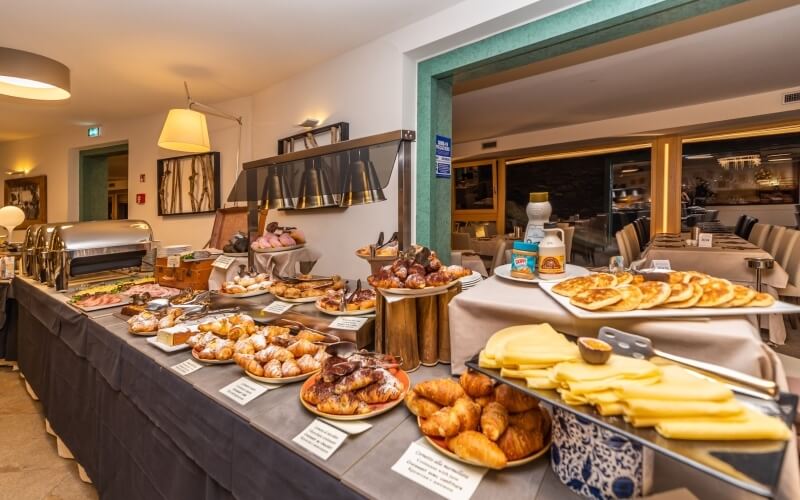 Buffet-style breakfast spread with pastries, pancakes, and cheese on a black tablecloth in a bright, inviting setting.