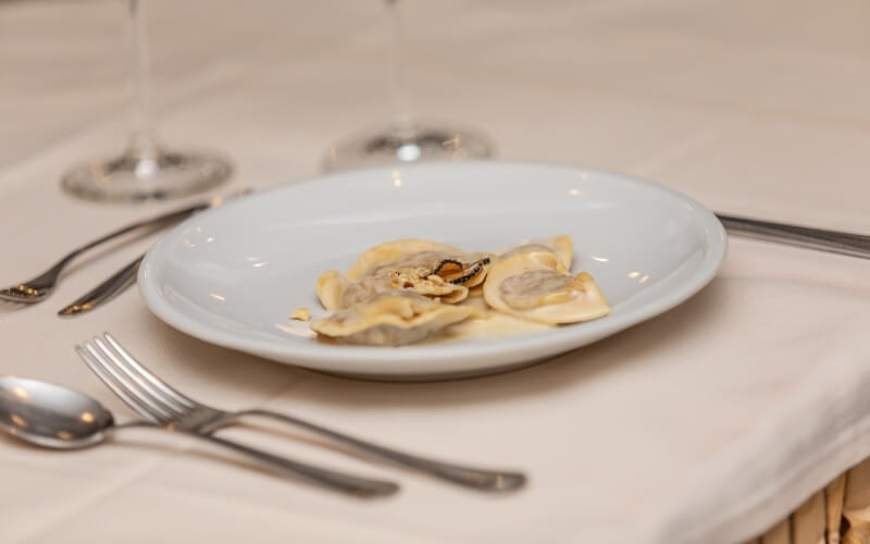 Table setting with a plate of pasta, wine glass, and utensils on a white tablecloth, suggesting a minimalist aesthetic.