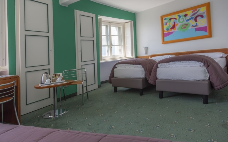 Cozy hotel room with two beds, a table, and a window, featuring modern decor and a green accent wall.