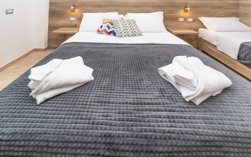 Cozy hotel room with two beds, white duvets, colorful pillows, wooden headboards, and light-colored wooden floor.