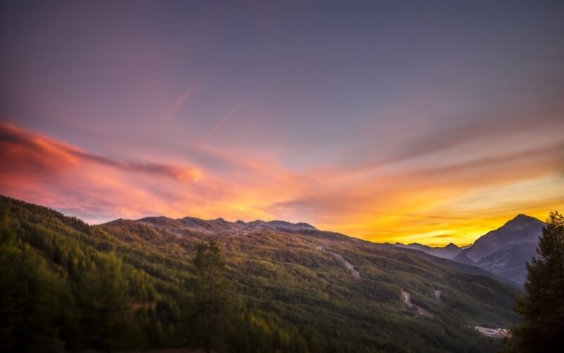 Catena montuosa verdeggiante al tramonto, con cielo colorato e sentiero che si snoda nel paesaggio sereno.