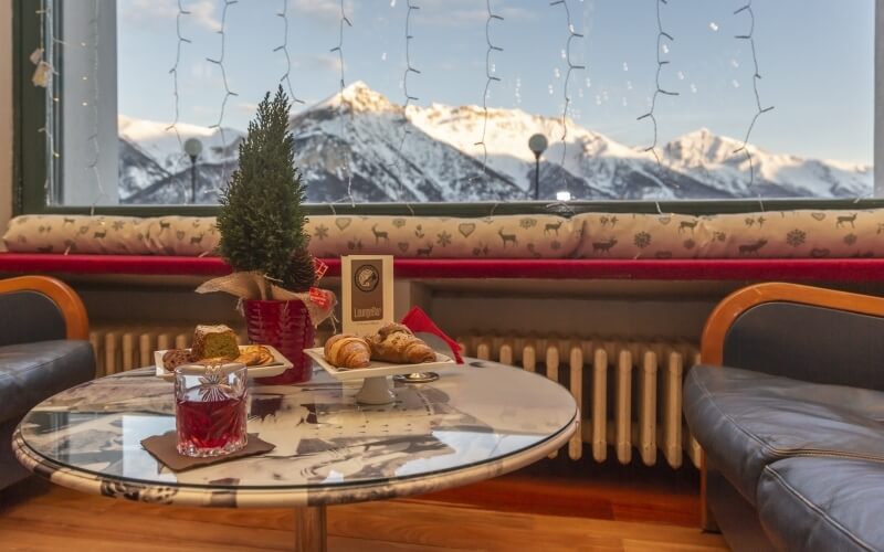 Cozy indoor setting with a red couch, Christmas decorations, and a view of snow-capped mountains through a large window.