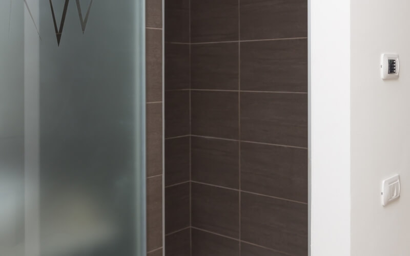 Modern bathroom section with frosted glass, etched "W" symbol, white walls, dark tile corner, and two thermostat-like devices.