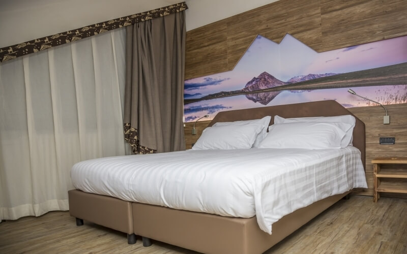 Cozy bedroom featuring a large bed, serene mural, wooden nightstand, and warm wood-paneled walls.