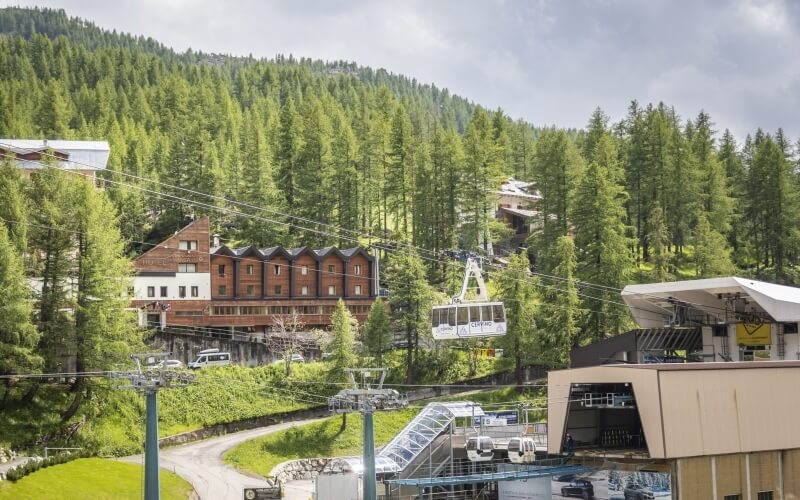 Serene mountainous landscape with a tan building, cable car system, and dense forest under an overcast sky.