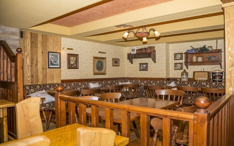 Rustic restaurant interior with wooden partitions, booths, tables, framed pictures, and a chandelier, creating a cozy atmosphere.