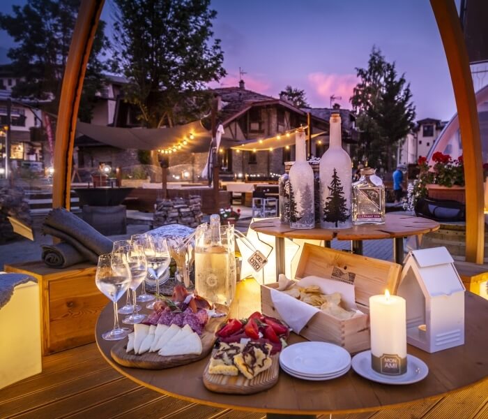 Un tavolo di legno circolare con cibo e bevande, circondato da un'atmosfera serena e un villaggio sullo sfondo.