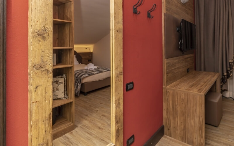 Cozy room with a bed and desk, red walls, wooden accents, and warm lighting, creating an inviting atmosphere.