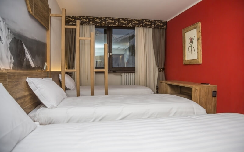 Cozy hotel room with two beds, red walls, wooden furniture, and a ladder leading to a loft area.