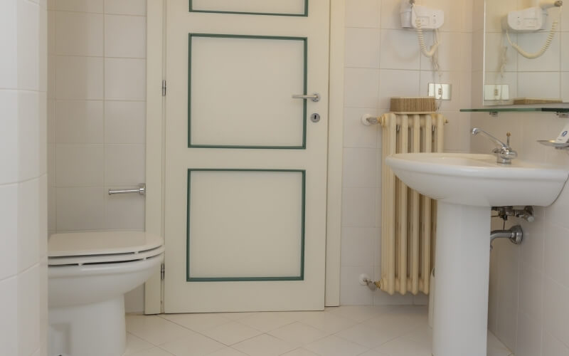 A clean bathroom with white walls, a left-side toilet, right-side sink, green-trimmed door, and a mirror above the sink.