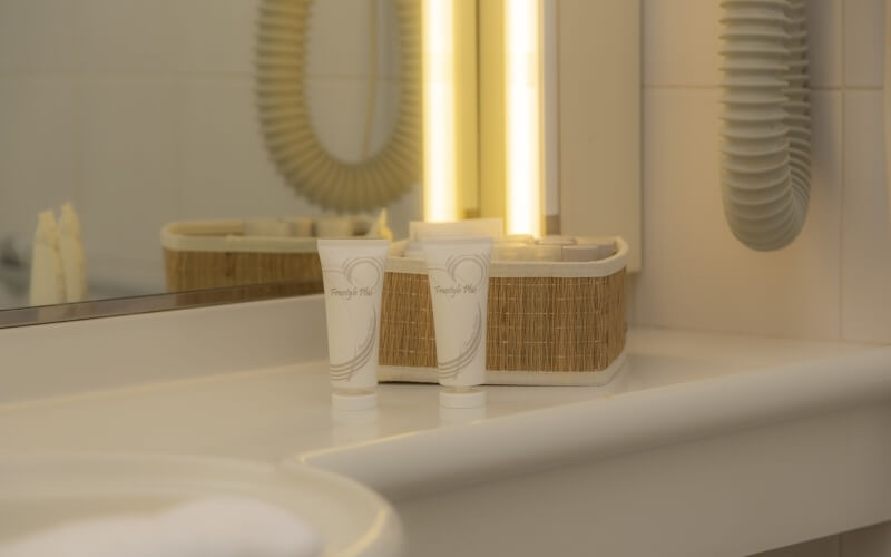 Immagine di un bagno con un lavabo bianco, tubi di crema, un cestino in rattan e uno specchio illuminato.