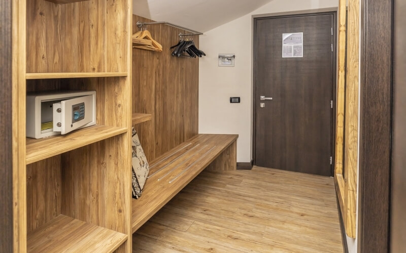 Compact room with wooden floors, built-in shelving, a white safe, floral pillow, and a brown door.