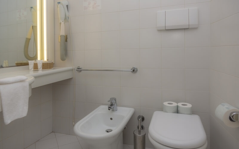 Clean bathroom featuring a white toilet, sink, mirror, toiletries, and tiled walls and floor.