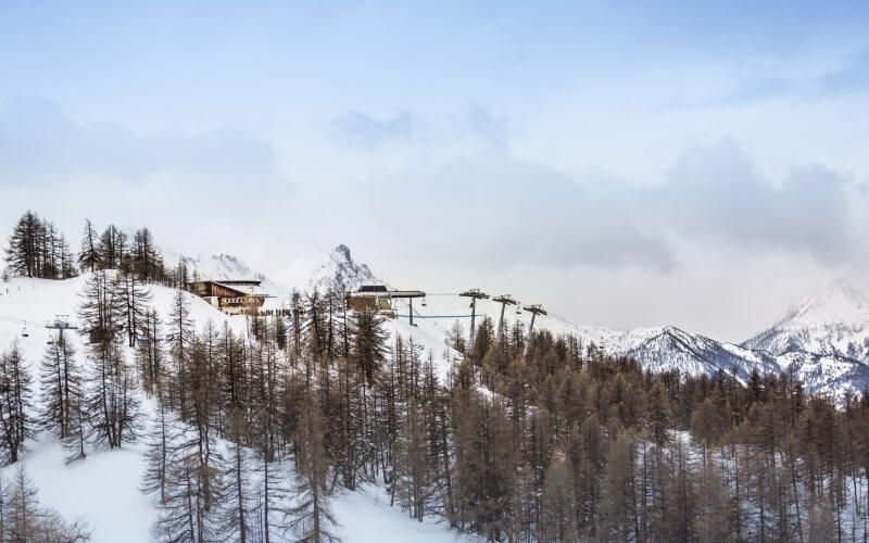 Scena invernale serena con montagne innevate, alberi, un edificio su una collina e impianti di risalita.